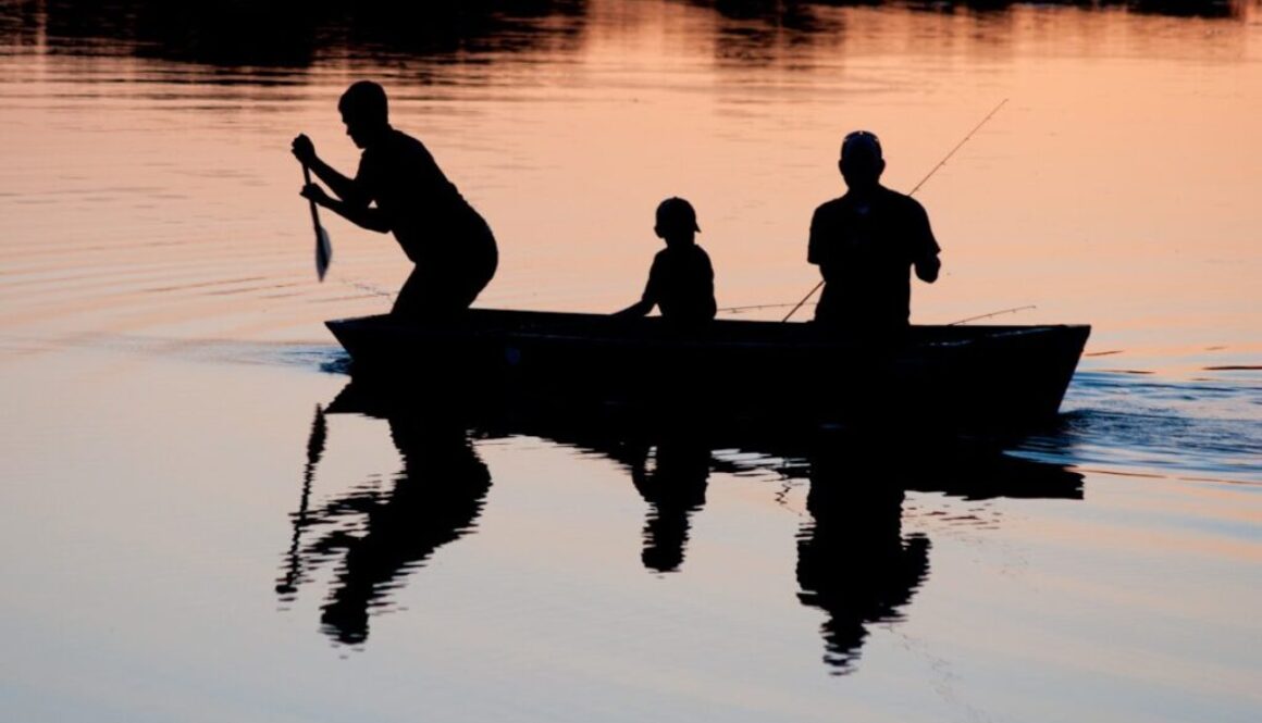 silhouette of three person riding on boat on body of water